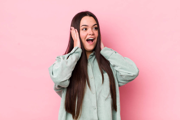 young adult woman feeling happy, excited and surprised, looking to the side with both hands on face - Photo, Image