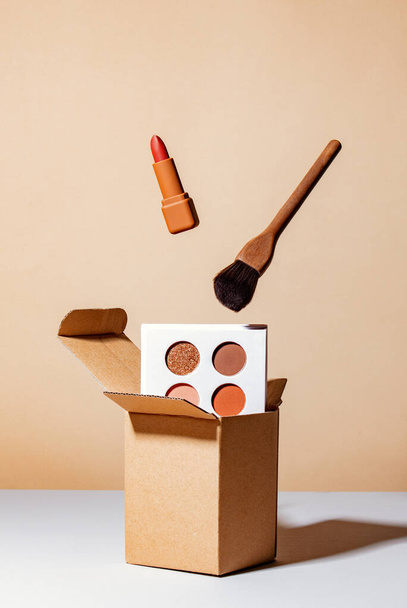 bruine luxe lippenstift en penseel zwevend over doos en tegen een bruine achtergrond - Foto, afbeelding