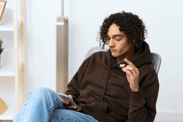 Um jovem sentado em uma cadeira com um telefone comunicação interior Estilo de vida. Foto de alta qualidade - Foto, Imagem