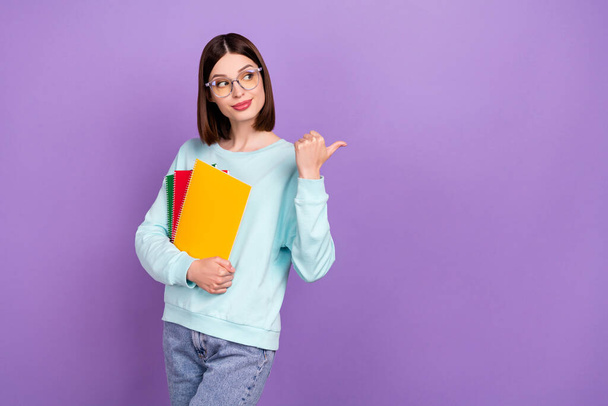 Photo portrait girl keeping book pile showing copyspace thumb isolated pastel purple color background. - Foto, afbeelding