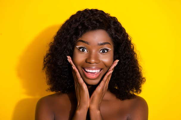 Photo of young happy excited smiling afro girl wear no clothes apply cream toner on cheeks isolated on yellow color background. - Foto, immagini