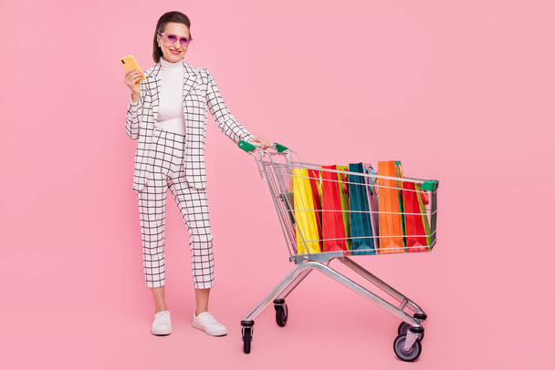 Full size photo of positive businesswoman go shopping in supermarket use smartphone isolated on pink color background. - Fotoğraf, Görsel