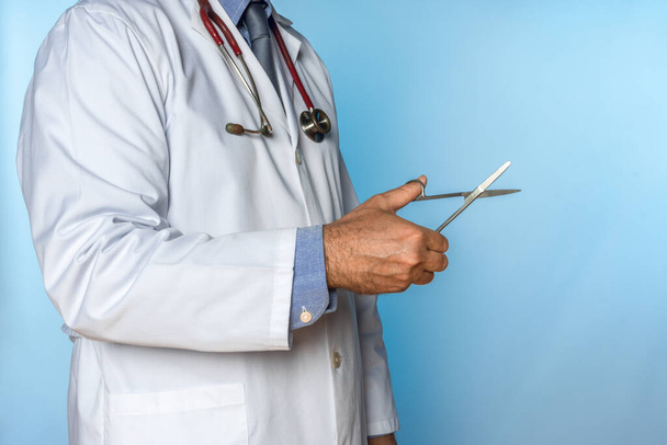médico com estetoscópio e tesoura na mão em um fundo azul - Foto, Imagem