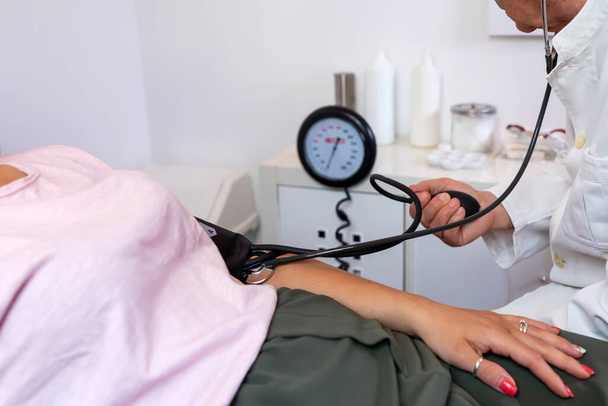 Doktor měří krevní tlak pacienta ležícího na lůžku v její kanceláři. Lékař měří krevní tlak pomocí rtuti sfygmomanometru. - Fotografie, Obrázek