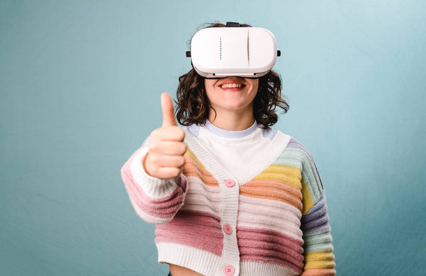 Nainen näyttää peukalo ylös, kun käytät VR virtuaalitodellisuus kuulokkeet yli sininen tausta. Teknologian käsite. - Valokuva, kuva