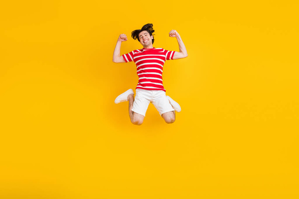 Full size photo of young positive man raise fists winner celebrate jump up isolated on yellow color background. - Фото, изображение