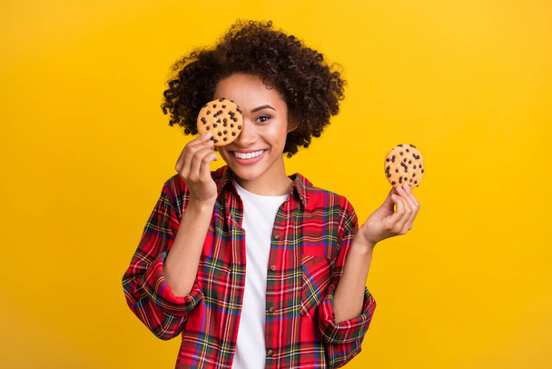 Portrait of attractive funny cheerful girl holding fresh delicious cookies closing eye isolated over bright yellow color background. - Photo, Image