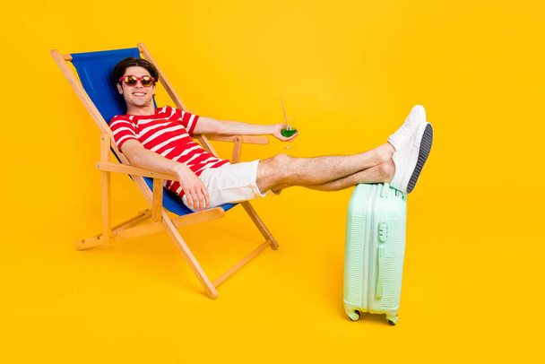 Photo of sweet charming man wear striped t-shirt sitting deck chair enjoying beverage smiling isolated yellow color background. - Photo, Image
