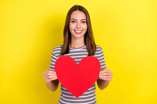Photo of lovely millennial brunette lady hold heart wear striped t-shirt isolated on yellow background. - Фото, изображение