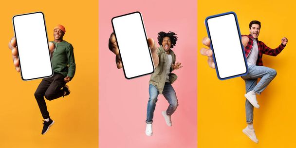 Три счастливых мультирасовых парня тысячелетия в случайном показе больших смартфонов с белым пустым экраном и празднование успеха на студийном фоне, весело, используя новейшее мобильное приложение, макет, коллаж - Фото, изображение