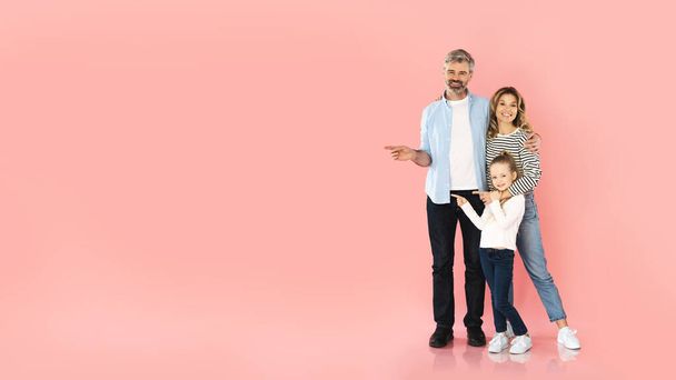 Rodina tří ukazující prsty vedle zobrazování volného místa pro text a reklama nabídka Usmívání se na kameru stojící objímání přes růžové pozadí. Studio Shot, Panorama - Fotografie, Obrázek