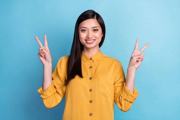 Photo of cool millennial brunette lady show v-sign wear yellow shirt isolated on blue color background. - Fotó, kép