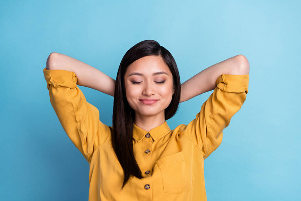 Photo of rest young brunette lady hands head wear yellow shirt isolated on blue color background. - 写真・画像