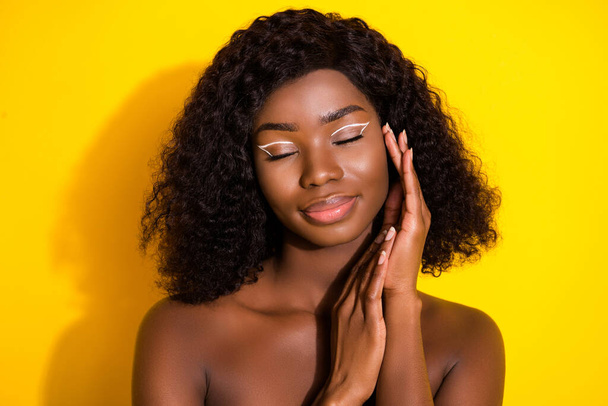 Photo of young beautiful peaceful african woman pampering applying cream on face isolated on yellow color background. - Photo, Image