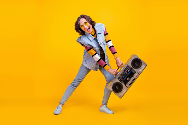 Full size photo of crazy white hairdo old lady hold boom box dance wear eyewear sweater vest jeans shoes isolated on yellow background. - Фото, зображення