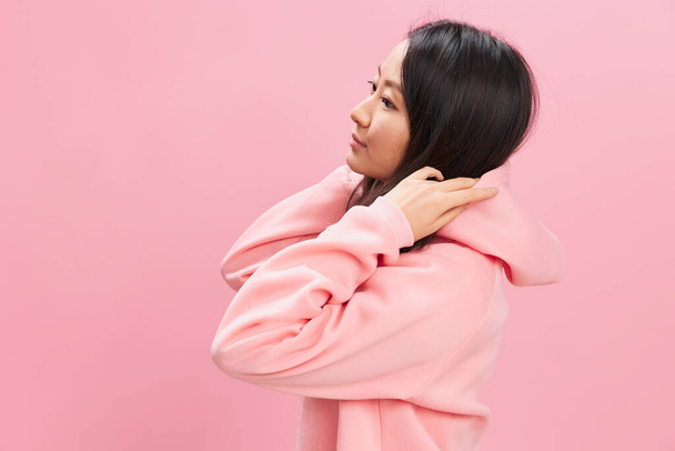Lado de vista linda estudante asiática jovem senhora em rosa camisola com capuz posando isolado sobre fundo estúdio rosa. Boa oferta para o anúncio. Conceito Fashion New Collection. Espaço de cópia - Foto, Imagem