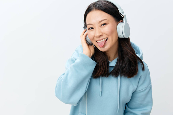 Śmieszne szczęście ładna koreańska młoda kobieta w niebieskim kapturze słuchawki wystawia język na kamerze pozowanie izolowane na ponad białym tle studio. Najlepsza oferta na reklamę. Koncepcja aplikacji muzycznej Platforma reklamowa - Zdjęcie, obraz