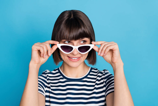 Photo of nice brunette young lady look empty space wear striped t-shirt sunglass isolated on blue color background. - Foto, afbeelding
