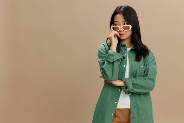 Happy nautti Korean nuori nainen khaki vihreä paita tyylikäs silmälasit näyttää syrjään poseeraa yli beige pastelli tausta. Siisti muotitarjous. Aurinkolasit mainos käsite - Valokuva, kuva