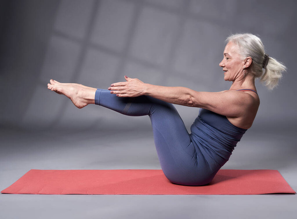 Senior woman with white hair training yoga, studio shot on gray background - Fotó, kép