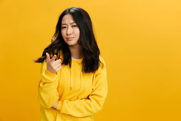 Hey, you. Confused incredulous cute Asian student young woman in yellow hoodie sweatshirt point finger at camera posing isolated on over orange studio background. Cool offer. People Emotions concept - Photo, Image