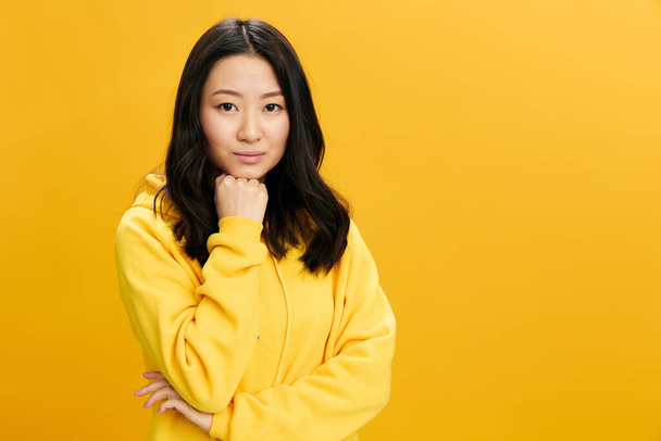 うーん どうした?。 黄色いフーディーのリクライニングで思慮深い年齢のアジアの学生の若い女性は,オレンジ色のスタジオの背景に隔離された教育上の問題について考えます. クールなオファー。 人々の感情コンセプト - 写真・画像