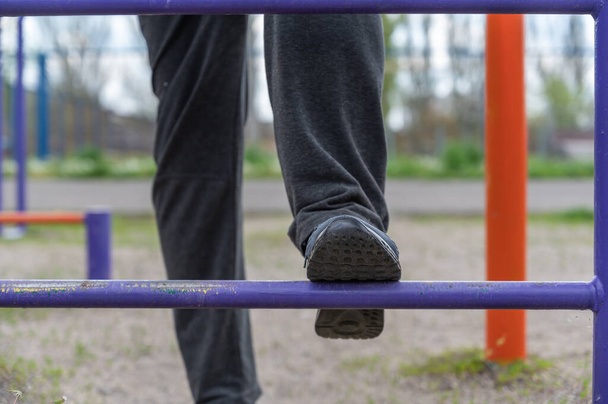 The lower section of a mature man doing gymnastics on an outdoor sports field. Legs of a man jumping on gymnastic equipment. Gymnastic exercises. Outside. Daytime. Selective focus. - Photo, Image