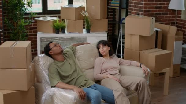 Marito stanco e moglie rilassarsi sul divano dopo aver disimballato i mobili per decorare lo spazio dell'appartamento. Trasferirsi in un nuovo appartamento in affitto insieme per iniziare un nuovo inizio di mutuo ipotecario. - Filmati, video