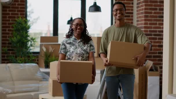 Portrait de couple afro-américain emménageant ensemble après avoir acheté un appartement en prêt hypothécaire. Regardant la caméra et se sentant heureux de déménagement, conteneurs en carton pour déplacer les meubles. - Séquence, vidéo