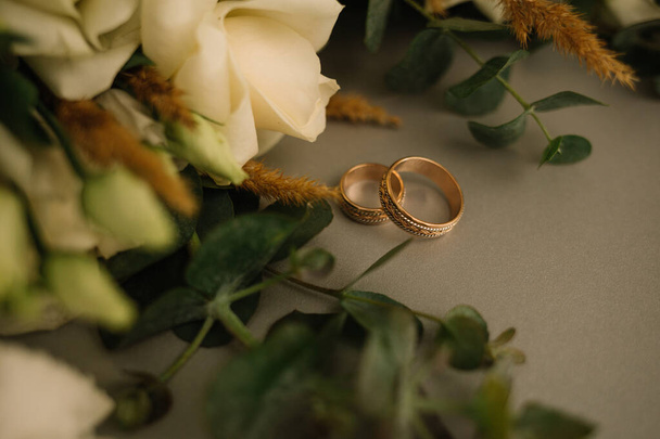 Two golden wedding rings and pink flowers on white background. Vertically framed shot. - Zdjęcie, obraz