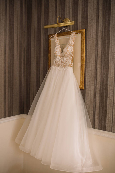 Hochzeitskleid hängt vor einem Wandhintergrund im Raum. Nahaufnahme. - Foto, Bild
