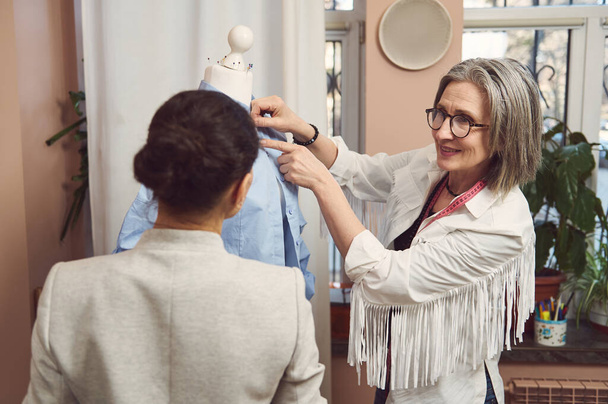 A skilled team of fashion designers tailors try on the new collection of women's dress shirt on a mannequin and work to improve the style and design of the new garments in the tailoring atelier - Photo, Image