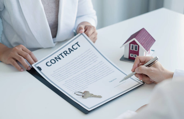 Ein Immobilienmakler mit einem Hausmodell spricht mit Kunden über den Kauf einer Hausversicherung und lässt sie Verträge im Rahmen des formellen Vertrages unterzeichnen. Wohnungsvermietung und Versicherungskonzept. - Foto, Bild