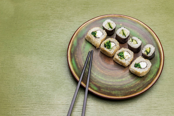 Sushi rolls and chopsticks on green plate. Soy sauce in bowls. Copy space. Top view. Green background - Valokuva, kuva