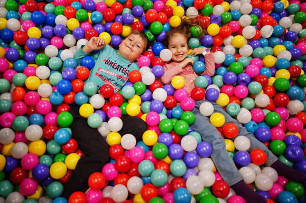 Brother with sister playing in colorful ball pit. Day care indoor playground. Balls pool for children. Kindergarten or preschool play room. - Photo, image