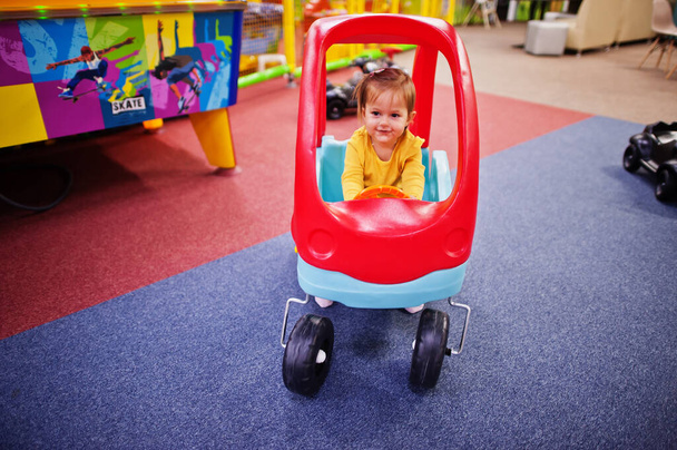 Cute baby girl rides on a plastic car in indoor play center. - Valokuva, kuva