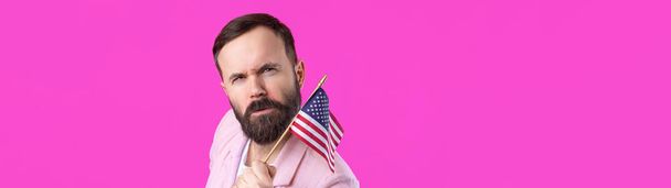 Portrait d'un jeune homme satisfait avec une barbe avec un drapeau américain sur fond de studio rouge. Grand patriote américain et défenseur de la liberté. - Photo, image