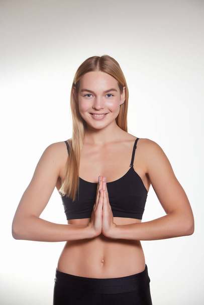 Instructor de yoga sonriente mostrando gesto namaste, entrenamiento en gimnasio, meditación en sportsbra y leggings, fondo blanco - Foto, Imagen