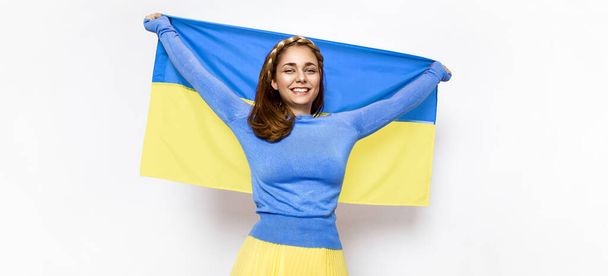Ukraińska dziewczyna nosi niebiesko-żółtą flagę Ukrainy trzepoczącą na białym tle. Flaga ukraińska jest symbolem wolności, wolności, demokracji, niepodległości i kursu europejskiego - Zdjęcie, obraz