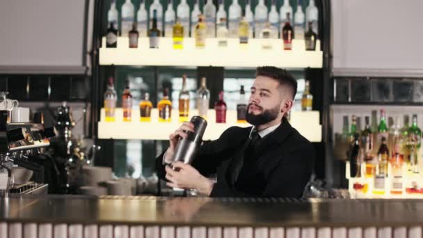 Knappe barman met baard in zwart pak en stropdas die alcohol maakt met speciale shaker. Blanke mannelijke barman bereidt cocktail volgens uniek recept in luxe restaurant. - Video