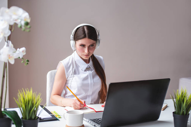 Focused millennial woman listening educational webinar, taking notes, getting remote online education at home. Female freelancer working on remote house. Woman in headphones learning language - Foto, Imagem