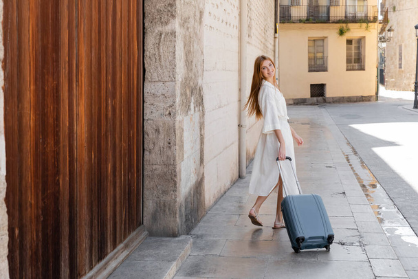 молодая веселая женщина в платье ходить с чемоданом на улице в Валенсии  - Фото, изображение
