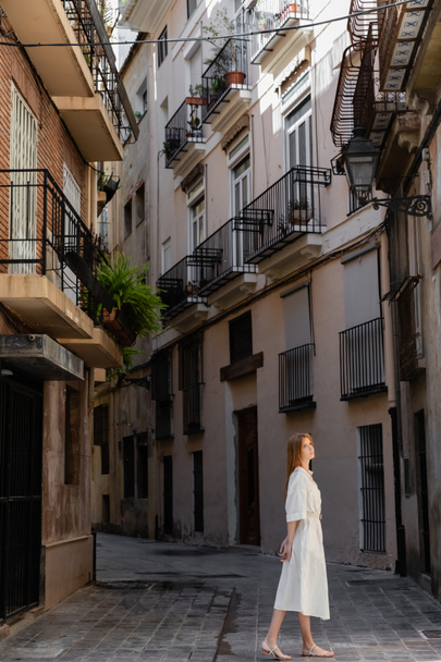 pelirroja vestida de pie cerca de casas en calle europea en valencia  - Foto, Imagen