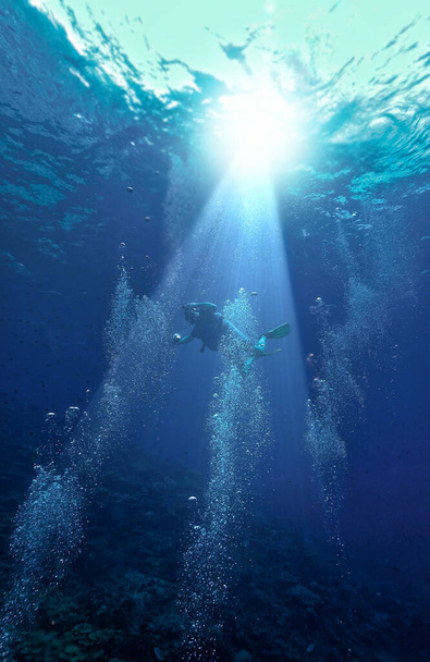 Unterwasserfotografie eines Tauchers im tiefblauen Meer bei schönem Licht und umgeben von Luftblasen. - Foto, Bild