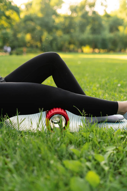 uma menina ao ar livre no parque entra para esportes em um esporte top roxo em leggings pretos em um tapete de esportes azul no fundo um prado e árvores - Foto, Imagem