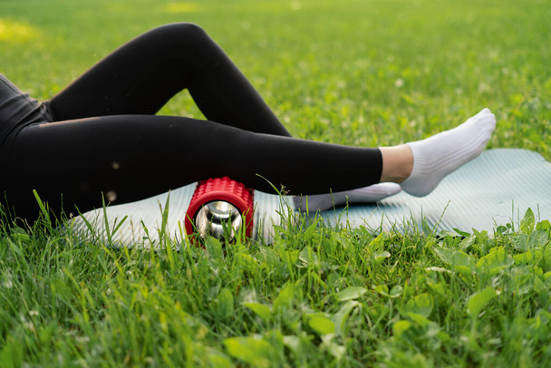 una ragazza all'aperto nel parco entra per lo sport in un top sportivo viola in leggings neri su un tappeto sportivo blu sullo sfondo un prato e alberi - Foto, immagini