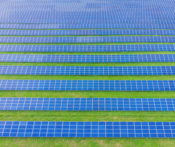 太陽光発電システムのドローンの空中ビュー。金属ブルーソーラーパネル、再生可能エネルギーおよび持続可能なエネルギー技術。代替エネルギー、緑の背景に行く. - 写真・画像
