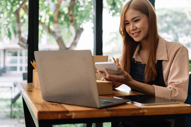 Ázsiai nő vállalkozó segítségével számológép ceruza a kezében, kiszámítja a pénzügyi költségek otthon iroda, online piac csomagolás doboz szállítás, Startup sikeres kisvállalkozás tulajdonosa, kkv, koncepció. - Fotó, kép