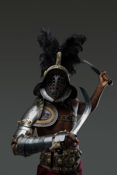 Studio shot van zwarte gladiator met gepruimde helm met twee zwaarden tegen grijze achtergrond. - Foto, afbeelding