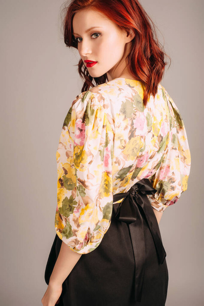 Female fashion. Redhead lady in elegant mini evening dress with long yellow balloon sleeves and black skirt on grey studio background. Young woman with red lips and natural hairdo. Holiday outfit. - Φωτογραφία, εικόνα